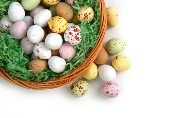 Obraz na płótnie Canvas Chocolate mini Easter eggs in straw or whicker basket against a white background