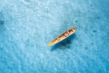 Aerial view of the fishing boat in transparent blue water at sunny day in summer. Top view from above of boat, sandy beach. Indian ocean in Zanzibar, Africa. Landscape with canoe and clear sea. Travel
