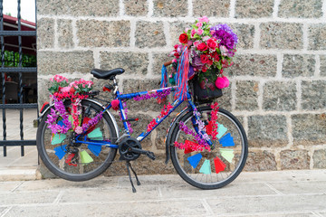 Fototapeta na wymiar Real bicycle decorated with plastic and fabric flowers leaned stone wall