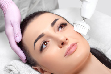 The cosmetologist makes the Hardware face cleaning  procedure with a soft rotating brush of a beautiful woman in a beauty salon. Cosmetology and professional skin care.
