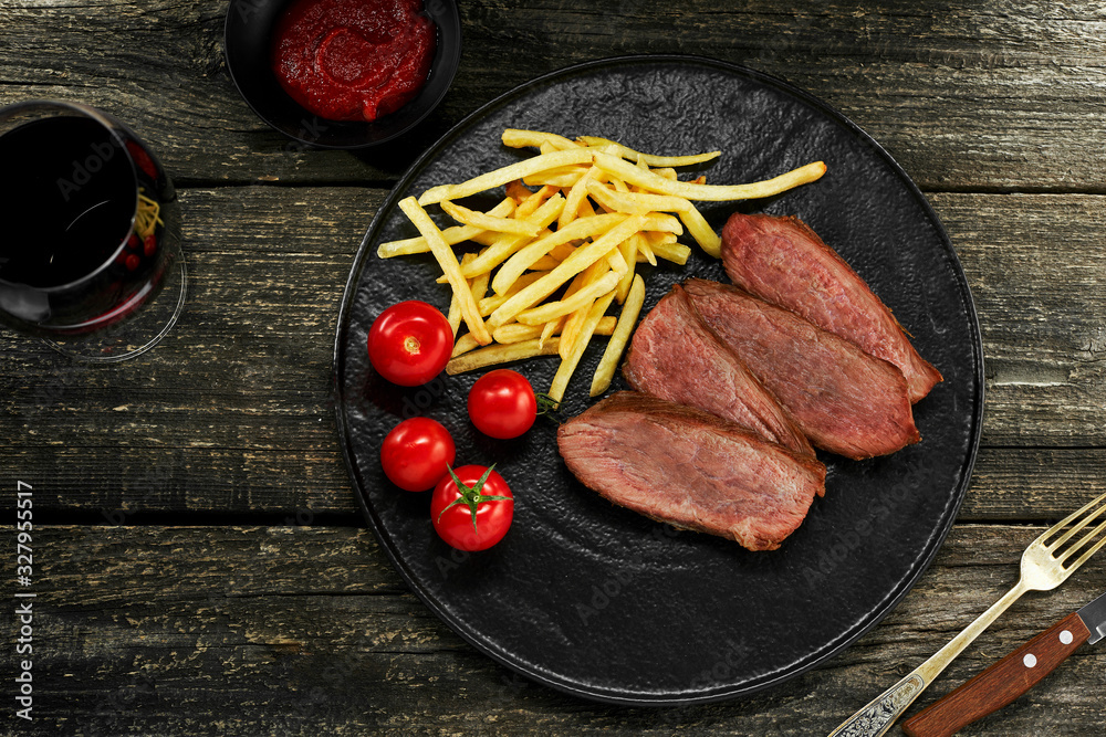 Wall mural steak with french fries, fresh cherry tomatoes, sauce and red wine on a rustic wooden table. wholeso