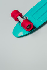 Green skateboard cruiser with red wheels on gray background with copy-space