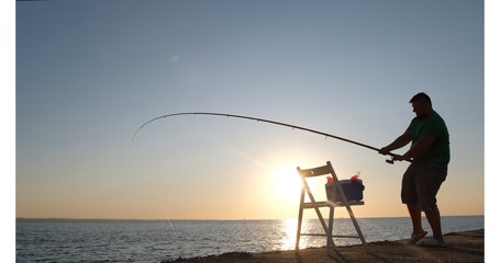 A plump man catches fish in the sea early in the morning.