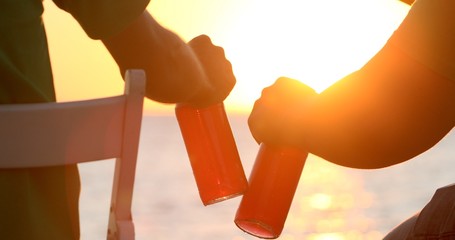 Two men fishing, sitting on chairs on a pier, and taking green bottles of beer in the morning sun.