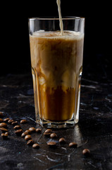 Iced coffee in a glass with pouring milk in black