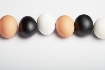 Row of eggs of different colors on a white background. Black, white and brown chicken eggs.