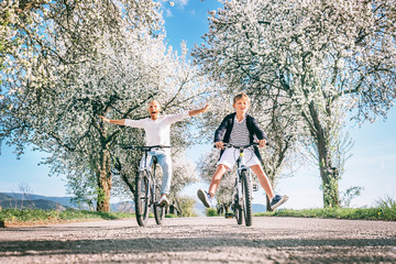 Obraz premium Father and son have a fun when riding bicycles on country road under the apple blossom trees. Free time spending with children concept image.