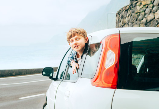 Blonde hair teenager boy look out from the rear passangers door of economy class auto and smiling.Rental car and Traveling by auto concept image.