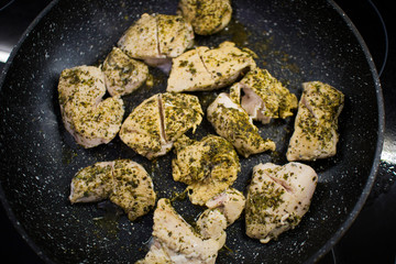 cooking chicken chopped in slices with herbs in a dark pan top view