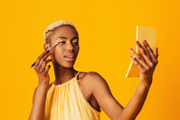 Portrait of a beautiful young woman applying yellow eye shadow make up to her eyes and holding compact mirror
