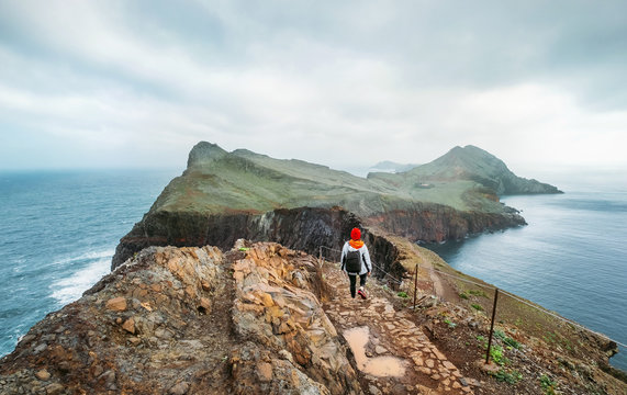 Young female backpacker hiking by footpath on Sao Lourenco headland with Atlantic ocean bay view in the end of February, Madeira island, Portugal. Active people around  World traveling concept image.