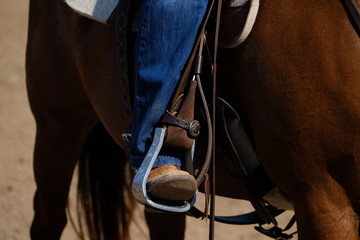 Western lifestyle shows close up of cowboy boot in aluminum stirrup while horseback riding. - obrazy, fototapety, plakaty