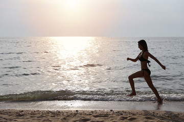 happiness on holiday silhouette side view image of young asian beautiful and sexy girl in black bikini who running on sandy beach in sunset on summer vacation