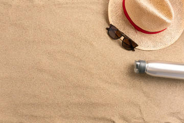 Fototapeta na wymiar Straw hat and bottle of water, on sand background. Beach vacation concept .Top view with copy space.