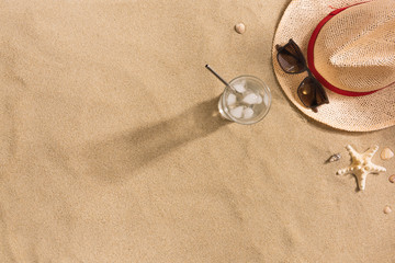 Fototapeta na wymiar Beautiful summer holiday beach background with straw hat, sunglasses, glass of water and shells on sand background, top view with copy space. Harsh shadows