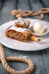 Apple strudel with caramel and nuts in icing sugar with a scoop of ice cream.