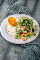 Sea salad of shrimp, avocado, tomato and cheese under arugula. On a turquoise background. Sea mood concept menu.