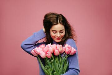 Girl holding bouquet of spring flower tulips against pink background. International womans day