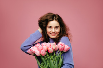 Girl holding bouquet of spring flower tulips against pink background. International womans day