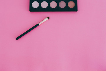 cosmetics products still-life, eyeshadow palette with brush on minimaist pink background and copyspace