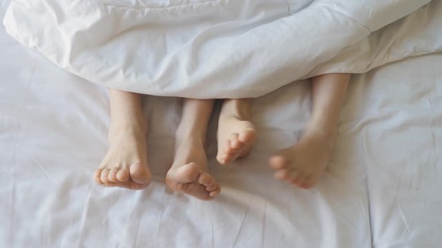 Two pair of feet next to each other in a bed. Mother and daughter lie on bed with white sheets.