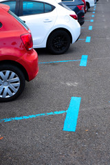 Cars parked in a residential parking zone marked with blue painted bands on the pavement of a big parking lot.