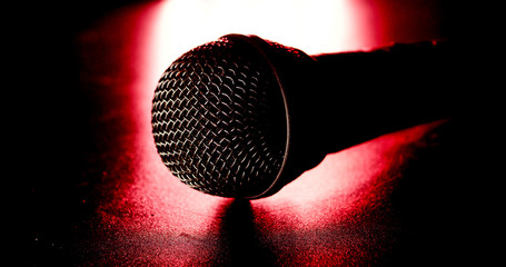 Close up of black microphone on a red light and black background.