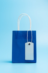 Single blue shopping or gift bag with blank label tag isolated on blue background