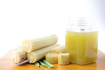 Fresh squeezed sugar cane juice in clear glass with cut pieces cane on white background.