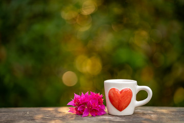 Cup coffee, pink flower on wooden table, spring nature bokeh background.