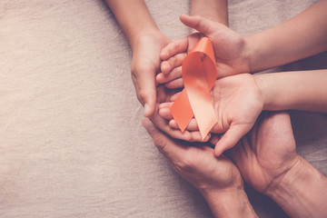 Adult and child hands holding orange Ribbons,  Leukemia cancer and Multiple sclerosis, COPD and ADHD awareness, world kidney day