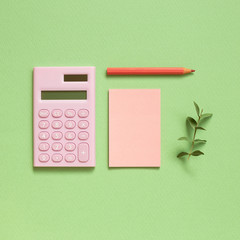 Pink digital calculator and memo note pad and colored pencil on pastel green background