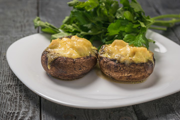 Baked mushrooms with cheese on a white plate with parsley leaves.