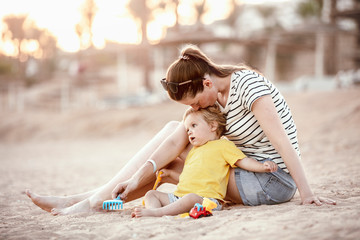 Happy mother and son playing on the beach. Mom and baby playing in the sand. Mom play with a toddler on the seaside. Lifestyle. Sunny day. Summer rest. Family vacation