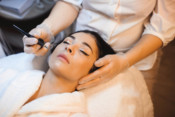 Obraz na płótnie Canvas Beautiful caucasian woman with black hair is having an anti acne procedure at the spa salon