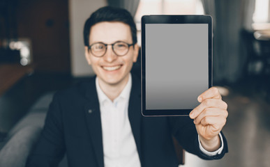 Smiling caucasian businessman dressed in a suit is showing a tablet with blank space