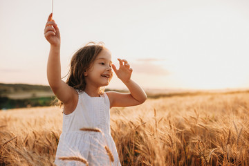 Smiling caucasian girl dressed in white dress is walking in a wheat field with a cheerful smile on leaps © Strelciuc
