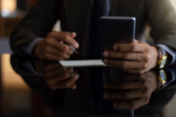Blurred image of business man in suit using mobile smartphone and plan to write and sign cheque at office.
