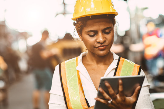 American women worker in heavy Industry maintenance engineer happy working wearing safety uniform and helmet using tablet computer to checking machine in factory.