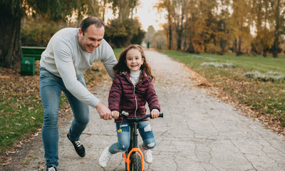 Balding caucasian father is teaching his daughter to ride the bike while walking together