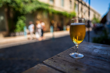 Full beer glass sitting on wooden picnic table in urban area in summertime