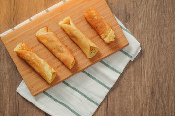 top view, filled pancake roll assorted flavors on bamboo chopping board placed on white and green striped cloth on wooden table