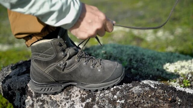 A hiker lacing his shoes. He is in tundra. He puts his foot on a rock.