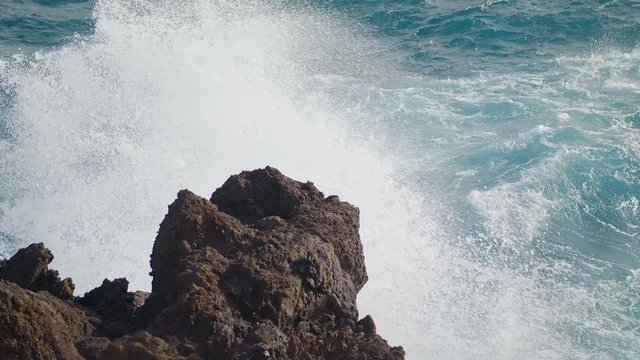Waves of Ocean Water crash on the rocks of the Volcanic island of Tenerife Clear Blue water of the Sea. Gale the Tide turns into pearl drops and splashes Waves reflect the sun's rays shot URSA 4.6K