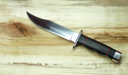 Bowie hunting knife on a wooden background. Combat army knife made of high- quality stainless steel. Weapons of attack and defense. The polished blade of the knife glitters. - obrazy, fototapety, plakaty