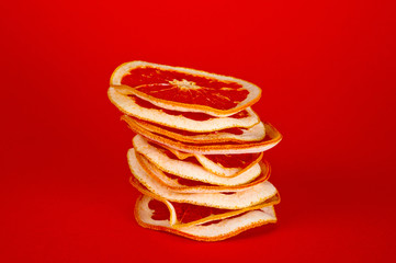 Chips of dried grapefruit sliced in thin circles, shot on a red background. Background for vegetarianism, healthy and wholesome food.