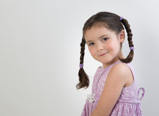 Preschool age girl in pink dress with cute expression and brown braids isolated on white background