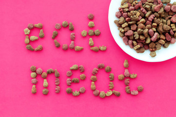 A bowl of cat food on a pink background with the inscription "eat meat" from pieces of cat food. The view from the top