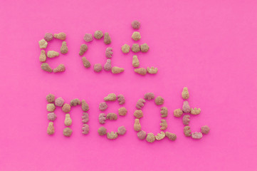 The inscription "eat meat" from pieces of food on a pink background. The view from the top