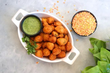 Moong dal ke pakode, ram laddoo, bhajias, Moongode or fritters. served with green mint and coriander chutney. Served over light background. Selective focus. with copy space.